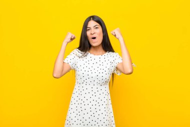 Genç ve güzel Latin bir kadın inanılmaz bir başarıyı kutluyor. Kazanan gibi, heyecanlı ve mutlu görünüyor. Al bakalım! yassı duvara karşı