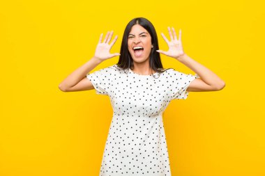 Genç, güzel, Latin bir kadın panik ya da öfke içinde bağırıyor. Şok olmuş, korkmuş ya da öfkeli. Elleri duvara dayalı.