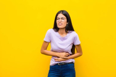 Genç, güzel, Latin bir kadın endişeli, hasta, hasta ve mutsuz hissediyor. Ağrılı bir mide ağrısı ya da duvarda grip geçiriyor.