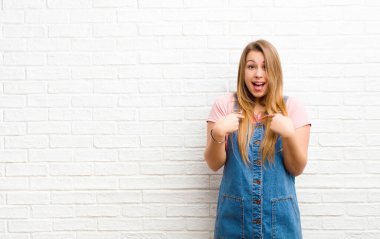 Genç sarışın kadın mutlu, şaşırmış ve gururlu hissediyor. Heyecanlı ve şaşkın bakışlarıyla tuğla duvara bakıyor.