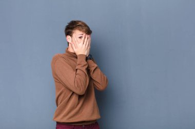 Genç sarışın adam korkmuş ya da utanmış hissediyor, dikizliyor ya da dikizliyor yarı çıplak elleriyle duvara yaslanmış.