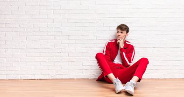 Genç sarışın adam mutlu bir şekilde gülümsüyor ve hayal kuruyor ya da şüphe ediyor, yere bakıyor.