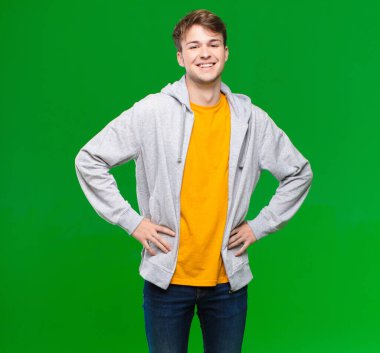 Genç sarışın adam mutlu, neşeli ve kendinden emin görünüyor. Gururla gülümsüyor ve iki elini de kroma tuşlu duvara yaslamış kalçasında görmek istiyor.