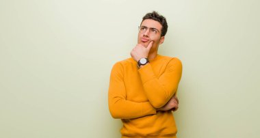 Genç Arap adam düşünüyor, şüpheci ve şaşkın hissediyor, farklı seçeneklerle, düz duvara karşı hangi kararı vereceğini merak ediyor.