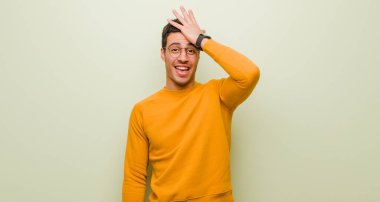 young arabian man raising palm to forehead thinking oops, after making a stupid mistake or remembering, feeling dumb against flat wall