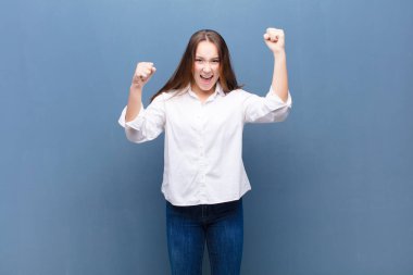 Genç sarışın güzel kız inanılmaz bir başarıyı kutluyor. Kazanan gibi, heyecanlı ve mutlu görünüyor. Al bakalım! beton duvara karşı