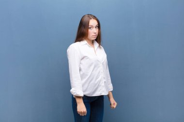 Aptal, çılgın, şaşırmış bir ifadeyle genç sarışın kız. Yanakları şişmiş, doldurulmuş, şişman ve beton duvarda yemek dolu.