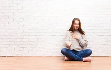 Genç sarışın güzel kız mutlu ve aşık, bir eli kalbinin yanında gülümsüyor ve diğer eli önde, yerde oturuyor.