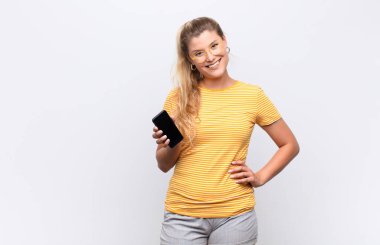 Genç ve güzel Latin bir kadın mutlu bir şekilde gülümsüyor, eli kalçasında ve kendine güvenen, pozitif, gururlu ve arkadaş canlısı bir tavır takınıyor.