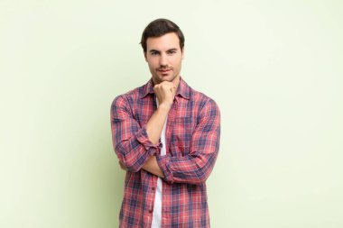 Genç yakışıklı adam mutlu görünüyor ve gülümsüyor. Elleri çenesinde, merak ediyor ya da soru soruyor. Seçenekleri karşılaştırıyor.