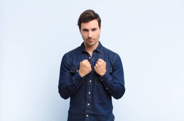 Kendinden emin, sinirli, güçlü ve agresif görünen bir adam. Yumrukları boks pozisyonunda dövüşmeye hazır.