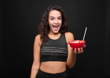 Genç ve güzel bir kadın mutlu ve hoş bir şekilde şaşırmış görünüyor. Büyülenmiş ve şok olmuş bir ifadeyle heyecanlı. Kahvaltıda sağlıklı bir kase yiyor.