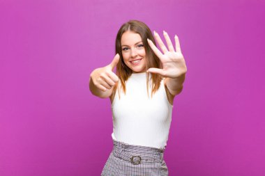 Kızıl saçlı güzel bir kadın gülümsüyor ve arkadaş canlısı görünüyor. Altı ya da altıncı numarayı gösteriyor. Elleri önde, mor duvara doğru sayıyor.