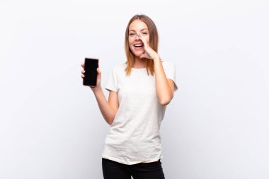 Kızıl saçlı, güzel bir kadın mutlu, heyecanlı ve pozitif hissediyor. Elleri ağızda, akıllı bir telefonla bağırıyor.
