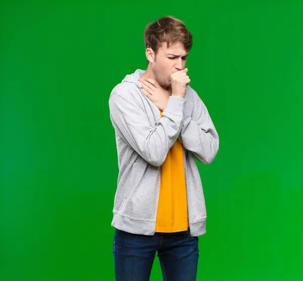 若いブロンドの男は喉の痛みとインフルエンザの症状で気分が悪くクロマキーウォールに覆われた口で咳をする — ストック写真