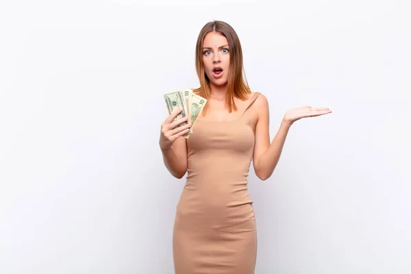 红头发的漂亮女人看上去很惊讶 很震惊 下颚掉了下来 手里拿着一个东西 旁边放着一只张开的手 上面有一美元钞票 — 图库照片