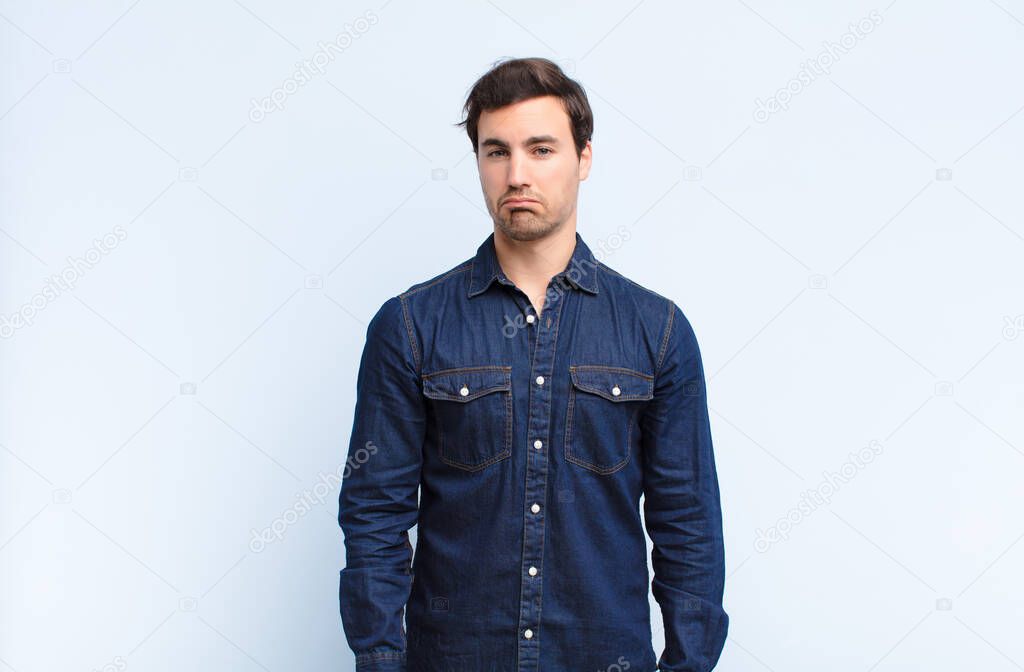 young handsome man feeling sad and stressed, upset because of a bad surprise, with a negative, anxious look against blue wall
