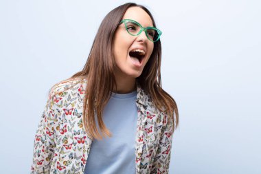 Genç ve güzel bir kadın öfkeyle bağırıyor, agresif bir şekilde bağırıyor, stresli ve sinirli görünüyor mavi duvara karşı.