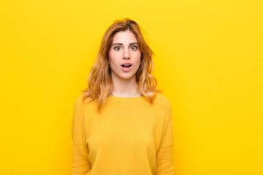 Genç, güzel sarışın kadın şok olmuş ya da şaşırmış görünüyor, ağzı açık sarı duvara karşı 