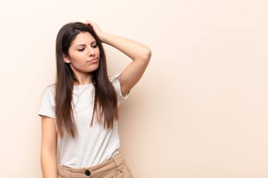 Genç, güzel bir kadın şaşkın ve kafası karışmış hissediyor, başını kaşıyor ve yan tarafa bakıyor.