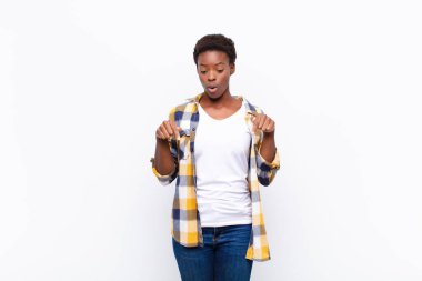 Genç, güzel, siyah bir kadın ağzı açık, iki eliyle aşağıya bakıyor, şaşkın, şaşkın ve şaşırmış görünüyor.