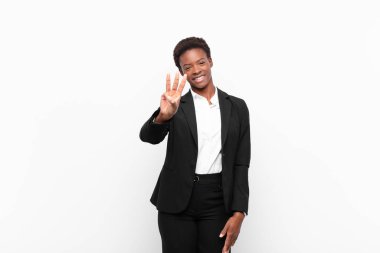 Genç, güzel siyah kadın gülümsüyor ve arkadaş canlısı görünüyor. Üç ya da üç numarayı gösteriyor. Elleri önde, beyaz duvara doğru sayıyor.