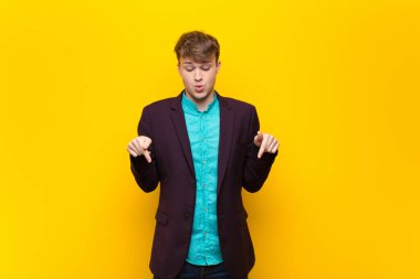 Genç sarışın adam, ağzı açık, iki eliyle aşağıya bakıyor, şaşırmış, şaşırmış ve şaşırmış görünüyor.