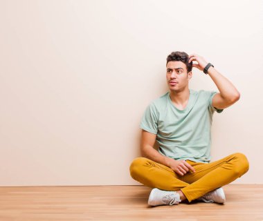 Genç Arap adam şaşkın ve kafası karışmış hissediyor, başını kaşıyor ve yere bakıyor.