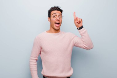 Genç Arap bir adam bir fikri fark ettikten sonra mutlu ve heyecanlı bir dahi gibi hissediyor, neşeli bir şekilde parmağını kaldırıyor, eureka! gri duvara yaslan