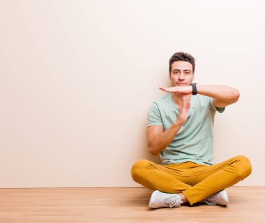 Genç Arap adam ciddi, sert, kızgın ve hoşnutsuz görünüyor. Yerde oturmuş zaman aşımına uğruyor.