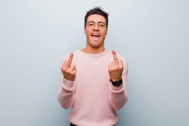 Genç Arap adam kışkırtıcı, agresif ve müstehcen hissediyor, gri duvara karşı isyankar bir tavırla orta parmağını hareket ettiriyor.