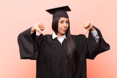 Genç Latin kız öğrenci üzgün, hayal kırıklığına uğramış ya da kızgın görünüyor, anlaşmazlık içinde başparmaklarını gösteriyor, hayal kırıklığına uğramış hissediyor.