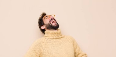 Genç havalı bir adam komik bir şakaya yüksek sesle gülüyor, mutlu ve neşeli hissediyor, düz duvara karşı eğleniyor.