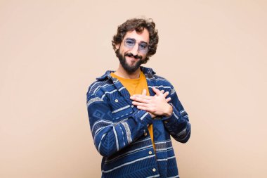 Genç çılgın adam romantik, mutlu ve aşık, neşeyle gülümseyen ve düz duvara karşı kalbe yakın el ele tutuşan