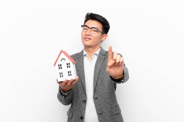 Genç Japon adam gururla ve kendinden emin bir şekilde gülümsüyor. Bir numaralı pozu başarıyla veriyor. Bir ev modeliyle lider gibi hissediyor.