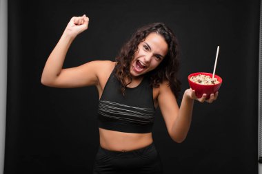 Genç ve güzel bir kadın sinirli bir ifadeyle ya da yumruklarıyla bağırarak kahvaltıda sağlıklı bir kase içerek başarıyı kutluyor.