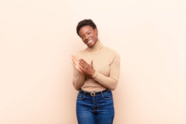 Genç siyah kadın mutlu ve başarılı hissediyor, gülümsüyor ve alkışlıyor, alkışlarla tebrik ediyor.