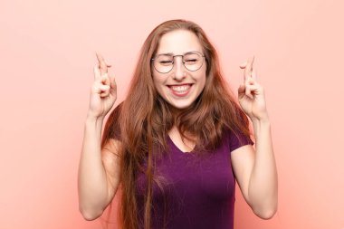 Genç sarışın kadın gülümsüyor ve endişeyle iki parmağını çapraz yapıyor. Endişeli ve iyi şanslar diliyor.