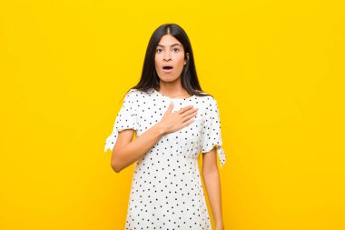 Genç ve güzel Latin bir kadın şok olmuş ve şaşırmış hissediyor, gülümsüyor, el ele tutuşuyor, o kişi olmaktan mutlu ya da düz duvara karşı minnettarlık gösteriyor.