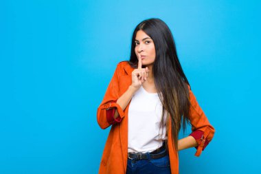 Genç ve güzel Latin bir kadın sessizlik ve sessizlik istiyor, parmaklarıyla ağzının önünde işaret ediyor, 