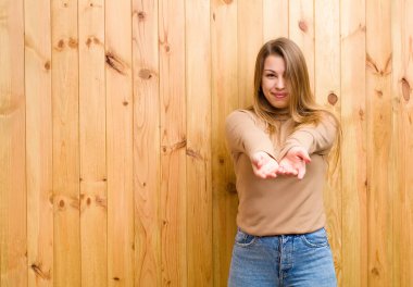 Genç sarışın kadın mutlu bir şekilde gülümsüyor arkadaş canlısı, kendinden emin, olumlu bakışlı, bir nesne ya da konsept sunuyor ve gösteriyor.