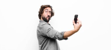 Genç çılgın adam akıllı telefonunu beyaz duvara karşı kullanıyor.