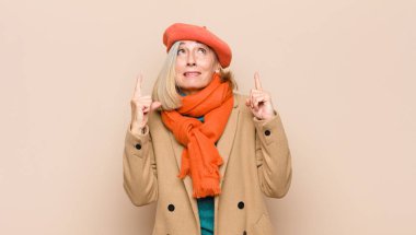 Yaşlı ya da orta yaşlı güzel bir kadın hayranlık duyuyor ve ağzı açık. Şok olmuş ve şaşırmış bir şekilde yukarı bakıyor.