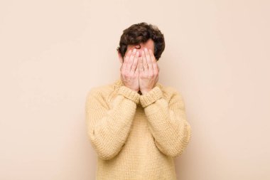 Havalı genç adam üzgün, hayal kırıklığına uğramış, gergin ve depresif, iki eliyle yüzünü örten, yassı duvara karşı ağlayan