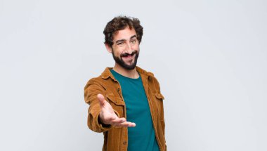 Genç yakışıklı adam gülümsüyor, mutlu görünüyor, kendinden emin ve arkadaş canlısı, anlaşmayı bitirmek için el sıkışma teklif ediyor, düz duvara karşı işbirliği yapıyor.