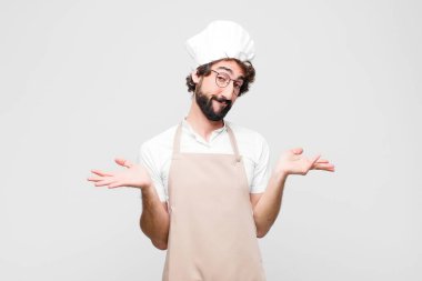 Genç çılgın aşçı şaşkın ve şaşkın hissediyor, doğru cevap ya da karardan emin değil, beyaz duvara karşı bir seçim yapmaya çalışıyor.