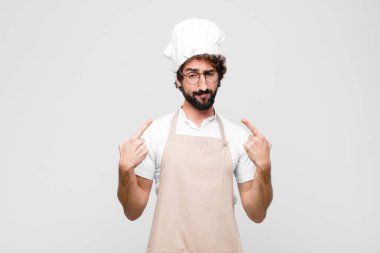 Kötü tavırlı genç çılgın şef gururlu ve agresif görünüyor, yukarı bakıyor ya da beyaz duvara yaslanmış ellerle alay ediyor.