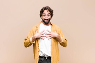 Genç çılgın havalı adam mutlu, şaşırmış, gururlu ve heyecanlı görünüyor, kendini düz duvara gösteriyor.