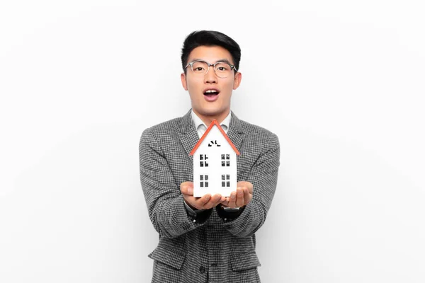 stock image young japanese man looking desperate and frustrated, stressed, unhappy and annoyed, shouting and screaming with a house model