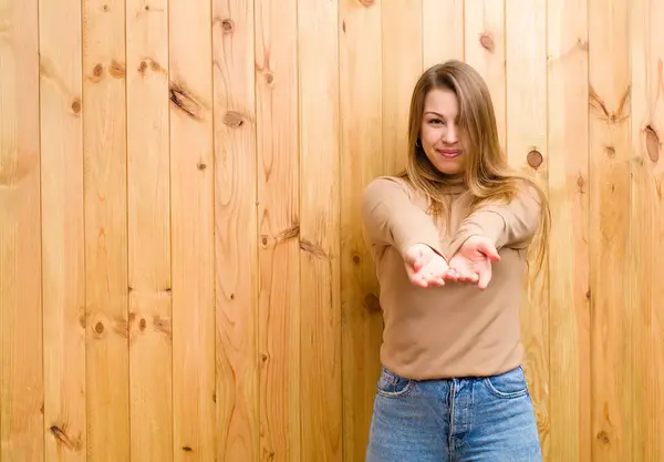 Genç sarışın kadın mutlu bir şekilde gülümsüyor arkadaş canlısı, kendinden emin, olumlu bakışlı, bir nesne ya da konsept sunuyor ve gösteriyor.
